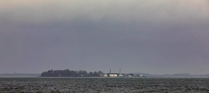 Lindholmin saari sijaitsee Etelä-Tanskassa parin kilometrin päässä lähimmästä rannasta keskellä Stegenlahtea. Virustutkimuskeskuksen vaaleat rakennukset näkyvät rantaan asti. (KUVA: JACOB CRAWFURD)