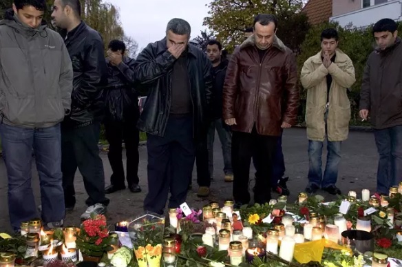 Ihmisiä kuvattuna Mohammad Ammourin surmapaikalla Linköpingissä vuonna 2004. Paikalla ovat murhatun isä Hassan (ruskea takki) sekä veli (vas.). Kuva: ARI LUOSTARINEN