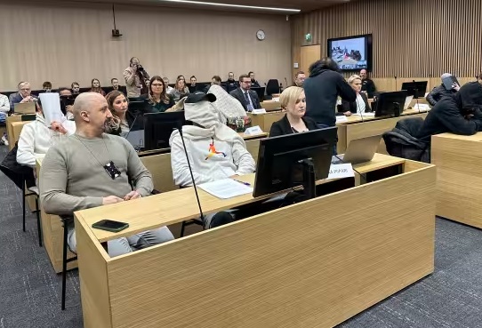 Osa syytetyistä peitti kasvonsa oikeudenkäynnin alussa. Kuvan vasemmassa reunassa oleva henkilö on tulkki. Kuva: Elisa Kinnunen / Yle.